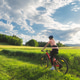 Female cyclist riding mountain bike on path through green fields Female cyclist riding mountain bike on path through green fields - PhotoDune Item for Sale
