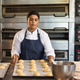 African American woman baker wearing chef coat holding tray with rolls by ovens and mixing bowl African American woman baker wearing chef coat holding tray with rolls by ovens and mixing bowl - PhotoDune Item for Sale