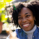Mid-adult African American woman smiling reaching for green leaves in sunny garden in denim jacket Mid-adult African American woman smiling reaching for green leaves in sunny garden in denim jacket - PhotoDune Item for Sale