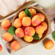 Top View Of Fresh Ripe Apricots In Wooden Bowl On Cutting Board With Green Leaves, Light Background Top View Of Fresh Ripe Apricots In Wooden Bowl On Cutting Board With Green Leaves, Light Background - PhotoDune Item for Sale