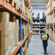 Warehouse worker in blue uniform holding a large cardboard box. Stacks of boxes are visible in the b Warehouse worker in blue uniform holding a large cardboard box. Stacks of boxes are visible in the b - PhotoDune Item for Sale