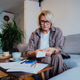 Middle aged woman reviewing expenses receipts while sitting on couch with coffee and phone in cozy l Middle aged woman reviewing expenses receipts while sitting on couch with coffee and phone in cozy l - PhotoDune Item for Sale