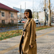 Young woman in a long brown coat with a camera walking on an autumn city sidewalk Young woman in a long brown coat with a camera walking on an autumn city sidewalk - PhotoDune Item for Sale